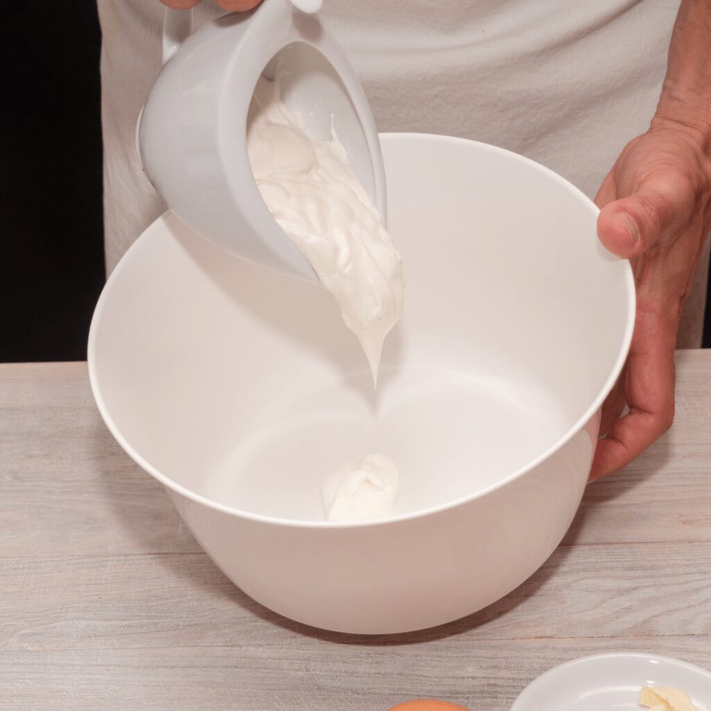 Making yogurt at home while carefully pouring the yoghurt from a into a bowl, set on a wooden table.