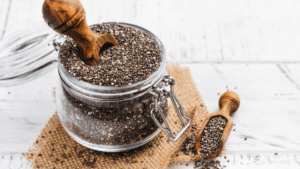 A clear glass bell jar filled with tiny, nutrient-rich chia seeds. The jar sits on a wooden surface, allowing the viewer to appreciate the contrast between the dark seeds and the transparent glass. The image visually communicates the concept of storing healthful foods in an aesthetically pleasing manner, emphasizing the importance of incorporating such superfoods into a balanced diet.