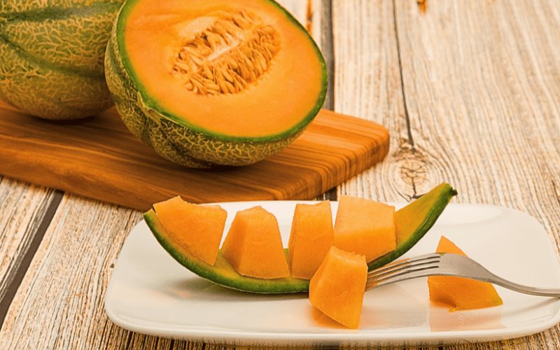 A halved cantaloupe is neatly displayed on a wooden cutting board, with succulent chunks up close captured against the backdrop of a rustic picnic table. The vibrant orange flesh of the cantaloupe exudes freshness and juiciness, while the intricate pattern of the seeds adds visual interest.