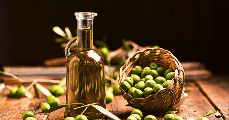 A glass bottle of premium olive oil, flanked by freshly picked olives cascading from a wicker bowl onto a rustic wood table.