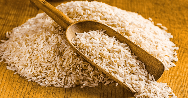 A wooden spoon heaped with fluffy jasmine rice, resting on a natural, textured wooden table