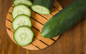 A whole, vibrant green cucumber rests gracefully on a rustic wooden table, exuding an air of freshness and natural appeal. Nearby, slices of cucumber are artistically arranged, showcasing the vegetable's crisp texture and refreshing essence against the warm, earthy backdrop.